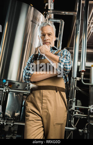 Fiducioso birraio senior in tute da lavoro in posa nella fabbrica di birra Foto Stock