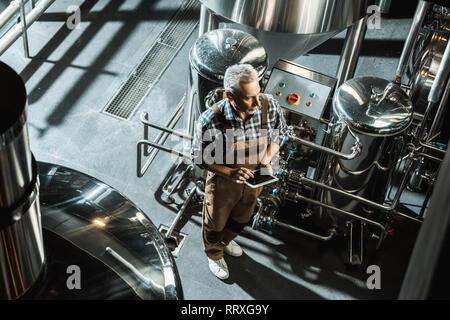 Vista aerea del fabbricante di birra in tute da lavoro con tavoletta digitale nella fabbrica di birra Foto Stock