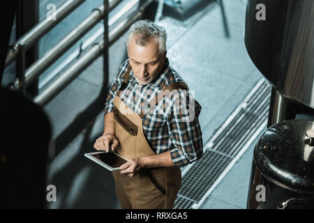 Vista aerea del produttore senior in tute da lavoro con tavoletta digitale nella fabbrica di birra Foto Stock