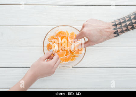 Vista ritagliata della giovane tenendo tangerine fette dalla ciotola di vetro bianco sul tavolo di legno Foto Stock