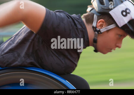 Determinata femmina atleta paraplegico accelerando lungo sport track durante la gara per sedia a rotelle Foto Stock