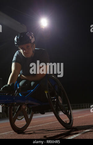 Ritratto determinata femmina e giovane atleta paraplegico formazione per sedia a rotelle gara su sport via di notte Foto Stock