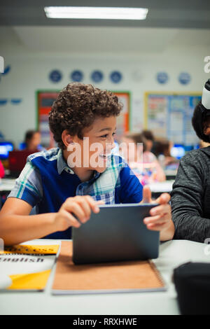 Felice scuola elementare boy utilizzando digitale compressa in aula Foto Stock