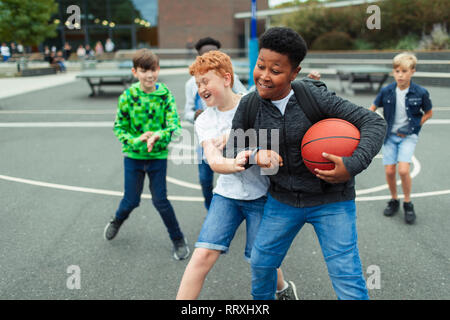 Tween ragazzi giocare a basket in schoolyard Foto Stock