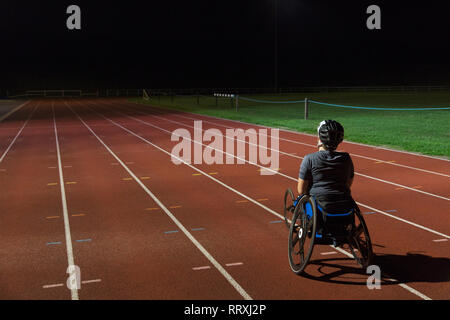 Determinata femmina atleta paraplegico formazione per sedia a rotelle gara su sport via di notte Foto Stock