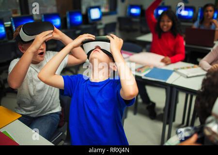 Curioso junior high school boys utilizzando la realtà virtuale simulatori in aula Foto Stock