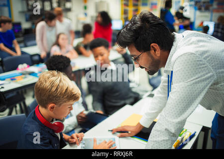 Insegnante maschio aiutando junior high school boy studente utilizzando digitale compressa in aula Foto Stock