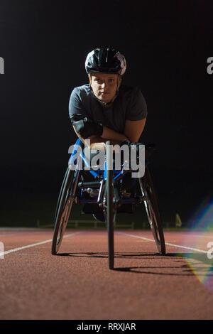 Ritratto determinato, resistente femmina e giovane atleta paraplegico formazione per sedia a rotelle gara su sport via di notte Foto Stock