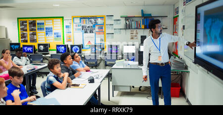 Insegnante maschio che conduce la lezione a schermo a sfioramento in aula Foto Stock