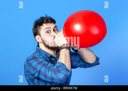 L'uomo il gonfiaggio di un palloncino rosso per bocca, Immagine su sfondo blu Foto Stock