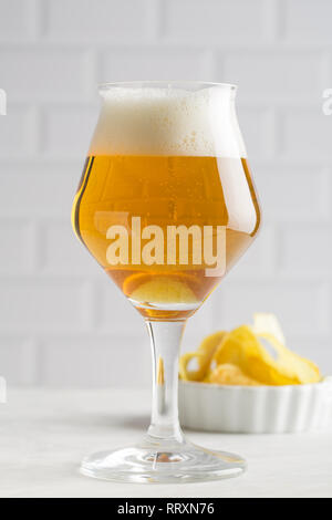 Bicchiere di birra e chips su sfondo chiaro Foto Stock
