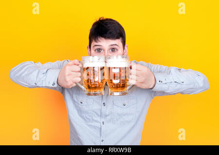 Divertenti uomo barbuto con grandi occhi, un ragazzo con due bicchieri di birra su sfondo giallo Foto Stock