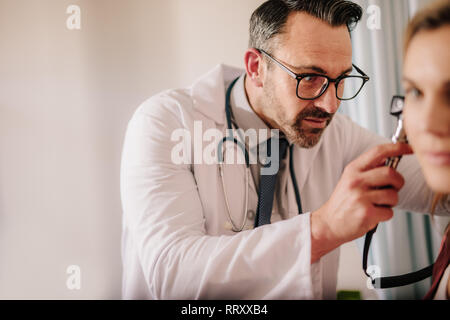 Medico maschio guardando femmina orecchio del paziente attraverso otoscopio. Il medico ORL facendo orecchio esame con otoscopio sul paziente . Foto Stock