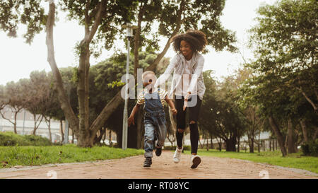 Giovane madre in esecuzione con little boy nel parco. Donna felice e carino kid avendo divertimento all'aperto. Foto Stock