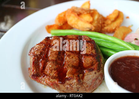 Chiuso fino alla brace bistecca di filetto con sfocato verdure cotte al vapore e patate fritte in background Foto Stock