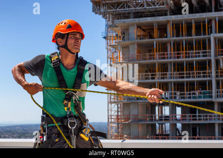 Alto edificio tecnico di corda di detergente per vetri sta lavorando su un sito in costruzione durante una soleggiata giornata estiva. Preso in Burnaby, Vancouver, BC, Canada. Foto Stock