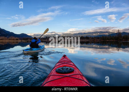 Uomo avventuroso kayak in acqua tranquilla durante un nuvoloso giorno d'inverno. Preso in Squamish, a nord di Vancouver, BC, Canada. Foto Stock