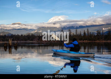 Uomo avventuroso kayak in acqua tranquilla durante un nuvoloso giorno d'inverno. Preso in Squamish, a nord di Vancouver, BC, Canada. Foto Stock