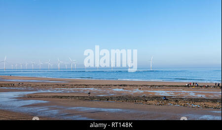 Una giornata di sole presso la costa a Redcar,l'Inghilterra,UK con gli studenti facendo il lavoro del corso sulla spiaggia e delle turbine a vento in background Foto Stock