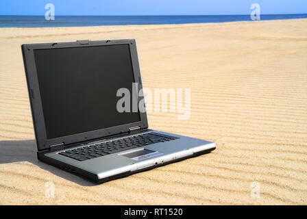 Laptop moderno giacente sulla sabbia. Spiaggia e pulire il cielo blu in background. Foto Stock
