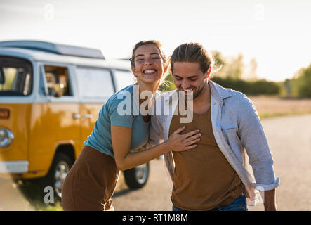 Coppia felice di fare un viaggio con un camper, abbracciando sulla strada Foto Stock