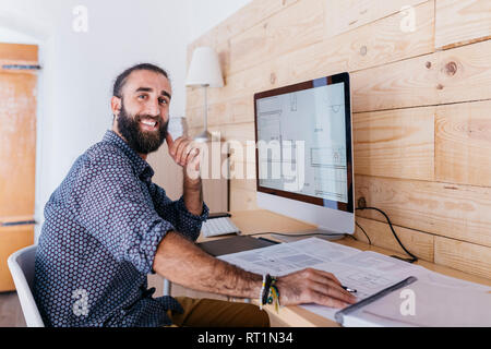 Ritratto di felice giovane architetto lavora a casa con blueprint e computer Foto Stock