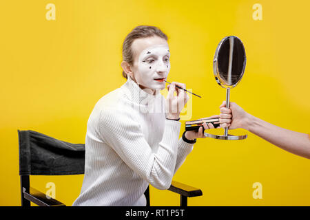 Attore di applicare il trucco per il viso per la pantomima sititng prestazioni in studio su sfondo giallo Foto Stock