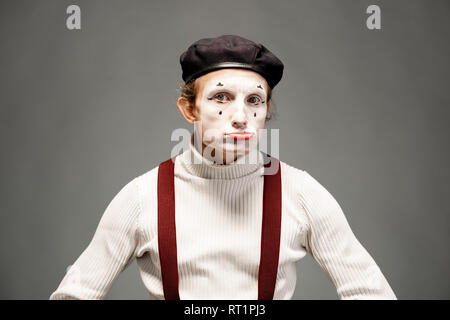 Ritratto di una pantomima attore bianco con il trucco per il viso in posa con espressive emozioni su sfondo grigio per interni Foto Stock