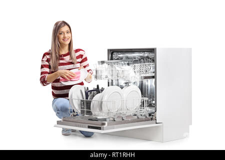 Giovane donna tergi una piastra accanto a una lavastoviglie e guardando la telecamera isolata su sfondo bianco Foto Stock