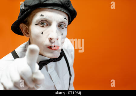 Ritratto di un attore come una pantomima bianca con il trucco per il viso mostra emozioni espressive su sfondo arancione in studio Foto Stock