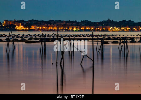 La fotografia notturna, una lunga esposizione immagine del cantiere e la zona industriale di Taranto, Italia con attrezzature di pesca nella parte anteriore e di acqua bella riflessi e colori del tramonto Foto Stock