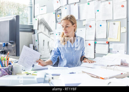 Donna seduta alla scrivania in ufficio per effettuare la documentazione Foto Stock