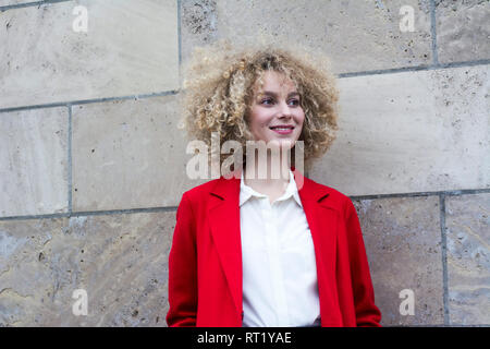 Ritratto di sorridere donna bionda con riccioli di indossare tuta rossa rivestire Foto Stock