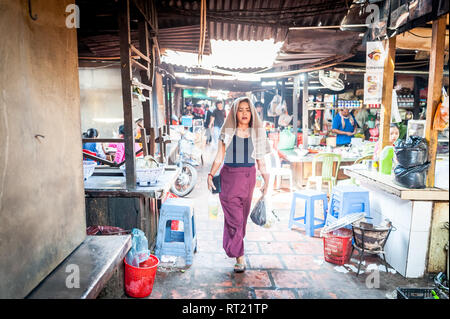 Una giovane signora fa il suo senso attraverso un mercato interno crampato occupato a Phnom Penh, Cambogia. Foto Stock