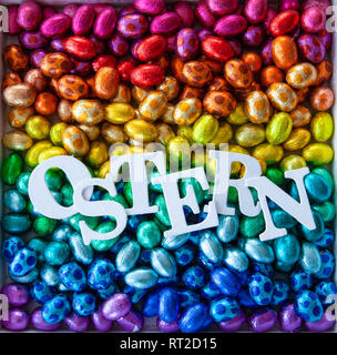 Allegro brillante di uova di cioccolato in arcobaleno di colori per una Felice Pasqua / Ostern si traduce per la Pasqua Foto Stock