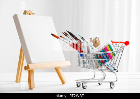 Mini carrello pieno di beni artistici per il disegno e la tela sul cavalletto. Negozio di arte concetto. Foto Stock