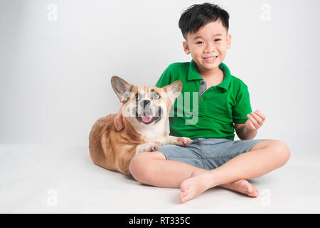 Ritratto di un gioioso little boy divertendosi con welsh corgi cane sul pavimento in studio. Foto Stock