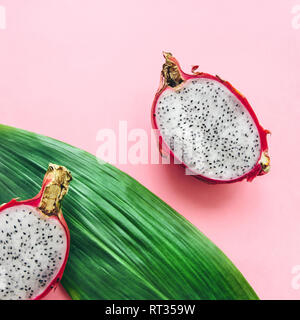 Dragon frutto di close-up photo due metà di un pitaya e una foglia di un albero di palma sono giacenti su un sfondo rosa laici piatta Foto Stock