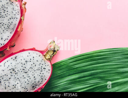 Dragon frutto top view photo due metà di un pitaya e una foglia di un albero di palma sono giacenti su un sfondo rosa modello con spazio di copia Foto Stock