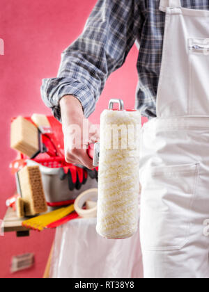 Giovani caucasici pittore casa lavoratore in bianco tute da lavoro, tiene il rullo con le mani. Industria edile. Sicurezza sul lavoro. Foto Stock