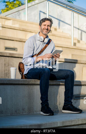 Ritratto di sorridere uomo maturo seduto sui gradini con la compressa Foto Stock