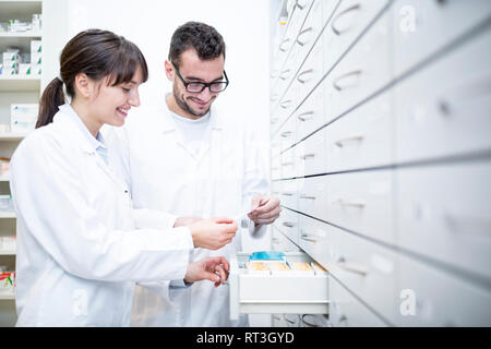 Due farmacisti sorridente con prescripiton ad armadio in farmacia Foto Stock