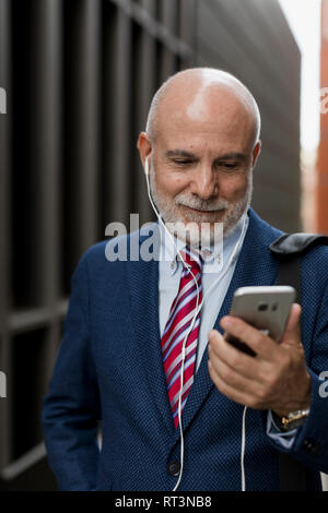 Imprenditore senior con un telefono cellulare e gli auricolari all'aperto Foto Stock