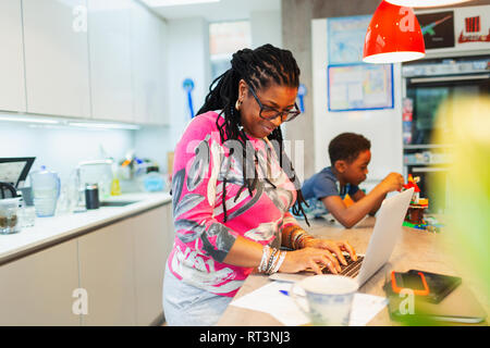 Donna matura utilizzando laptop in cucina Foto Stock