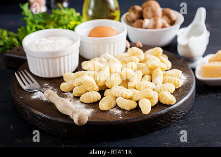 Non cotte Gnocchi fatti in casa con salsa alla panna funghi porcini e prezzemolo nel recipiente su uno sfondo scuro. Foto Stock