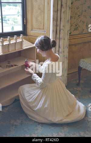 La Principessa Victoria gioca con le sue bambole casa a una finestra nella sua camera da letto a Kensington Palace. Indossa un abito bianco e ha i suoi capelli in un panino. Foto Stock