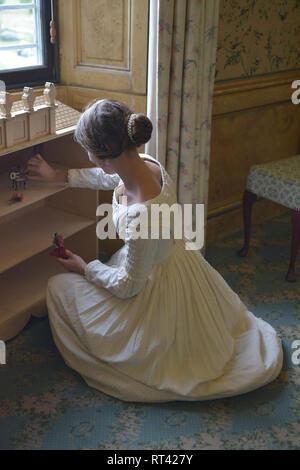 La Principessa Victoria gioca con le sue bambole casa a una finestra nella sua camera da letto a Kensington Palace. Indossa un abito bianco e ha i suoi capelli in un panino. Foto Stock