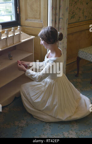 La Principessa Victoria gioca con le sue bambole casa a una finestra nella sua camera da letto a Kensington Palace. Indossa un abito bianco e ha i suoi capelli in un panino. Foto Stock