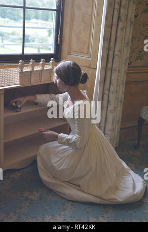 La Principessa Victoria gioca con le sue bambole casa a una finestra nella sua camera da letto a Kensington Palace. Indossa un abito bianco e ha i suoi capelli in un panino. Foto Stock