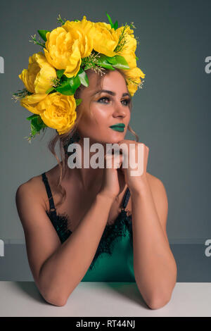 Ritratto di un simpatico bella bionda con un cerchio di fiori di colore giallo e brillante trucco su sfondo scuro Foto Stock